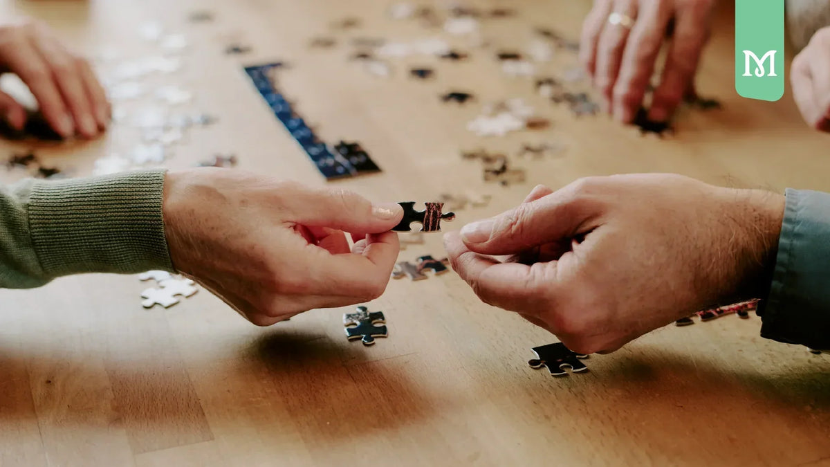 a hand passing a puzzle piece to another hand on a table