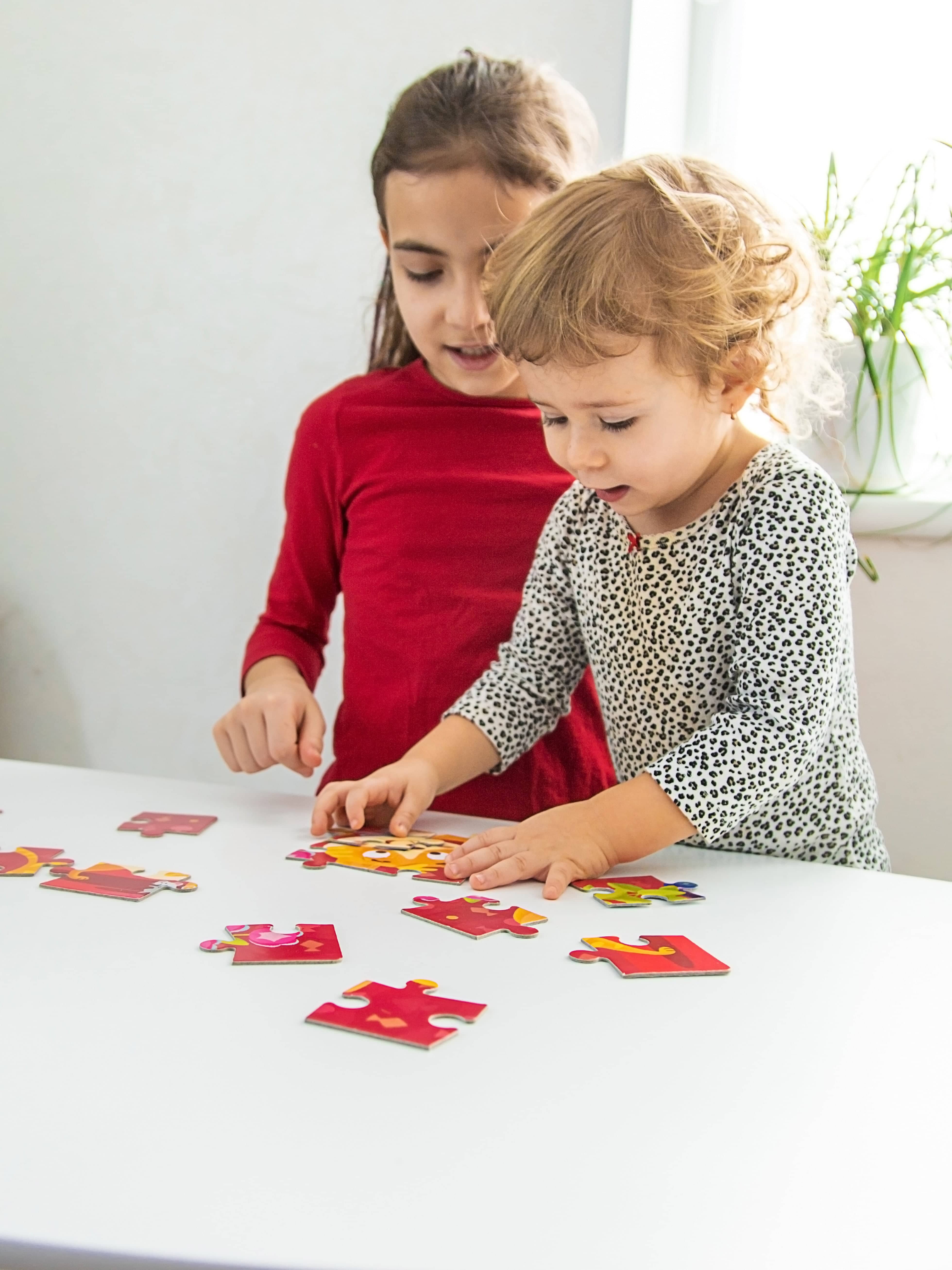 Two children playing with colorful puzzle pieces on a white table.