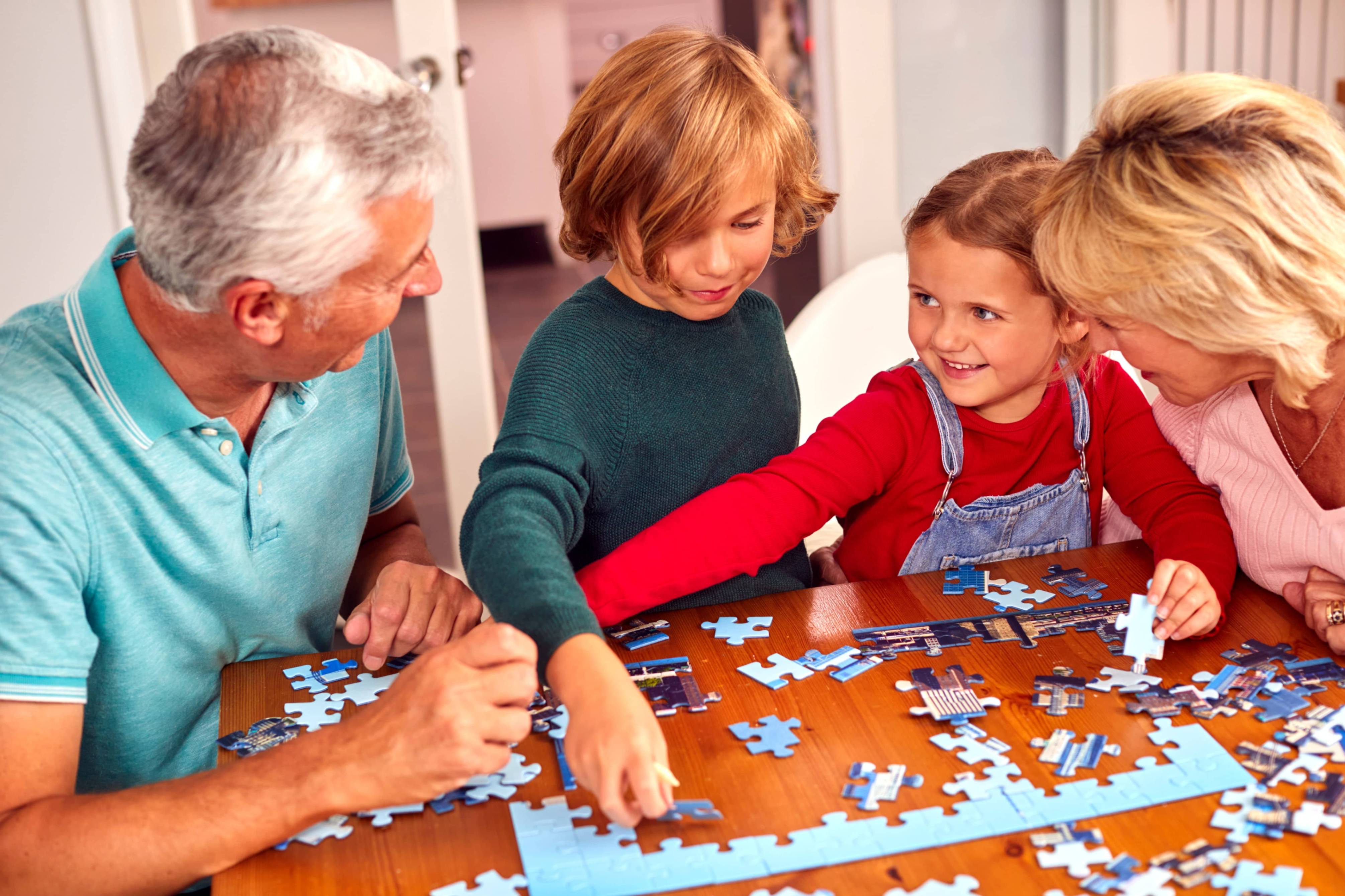 Family of four, including grandparents and two children, working on a puzzle together at a table.