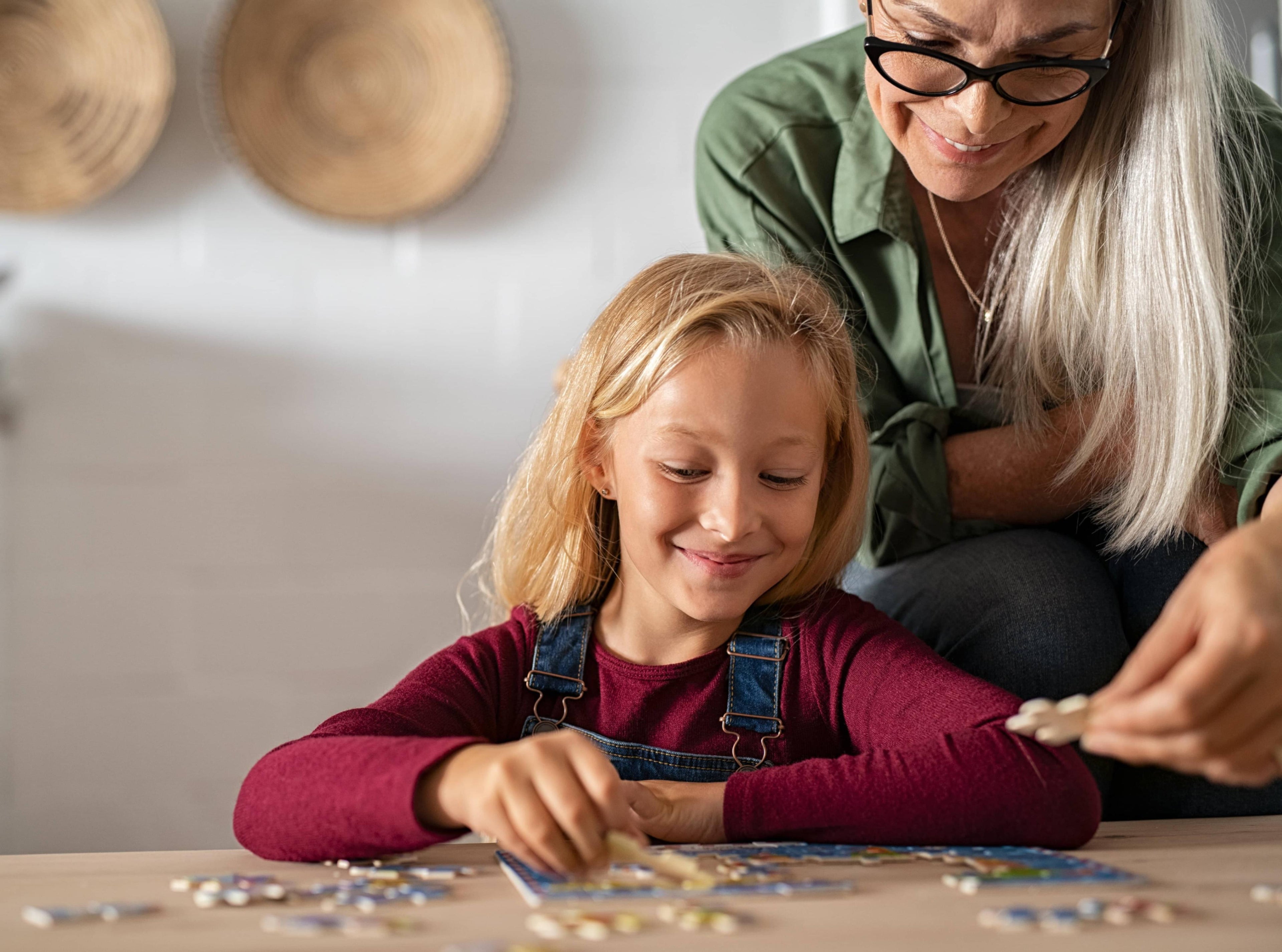 Woman and young girl playing with puzzle pieces on a table.